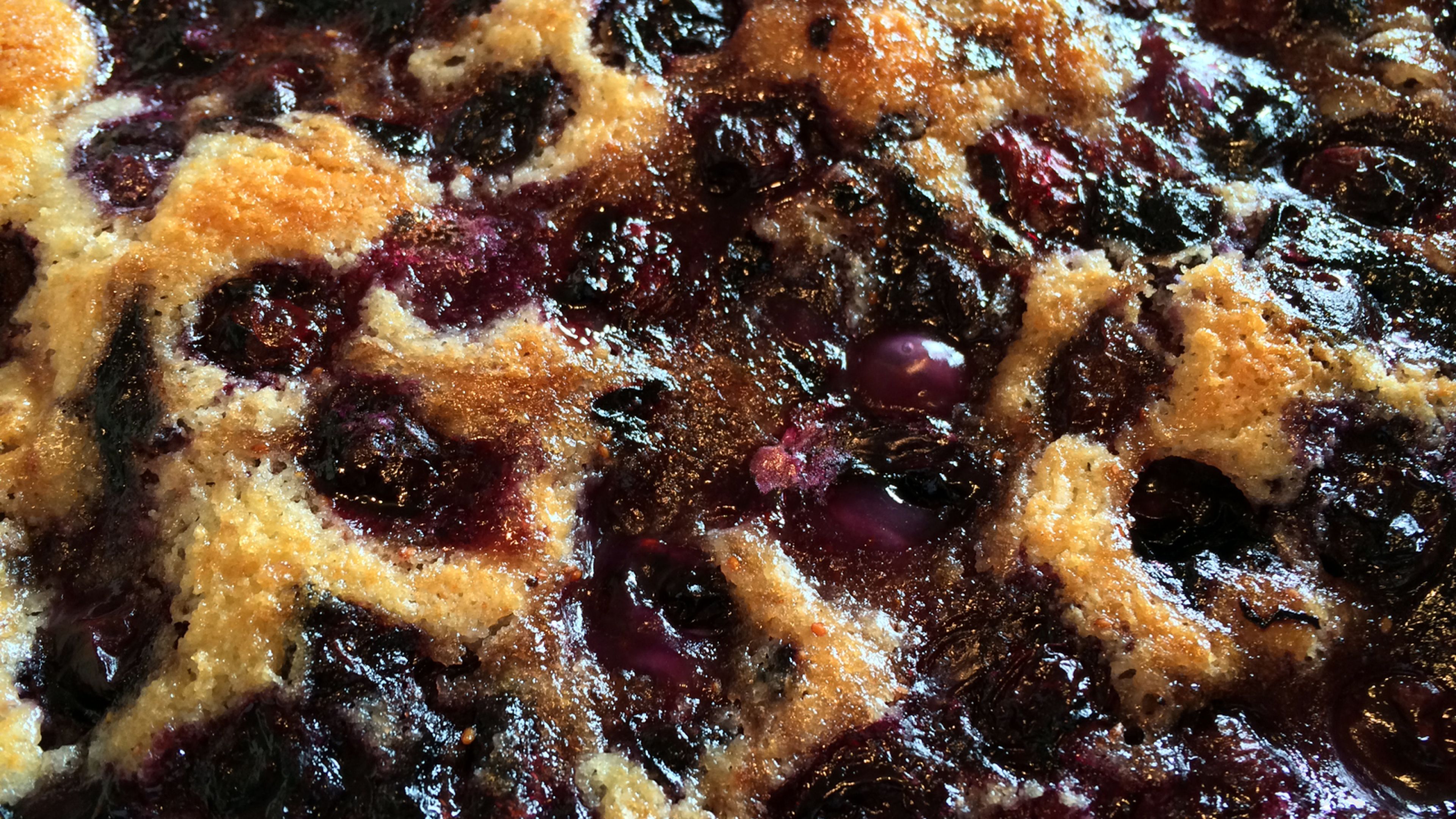 Golden-brown berry cobbler cake with a crispy sugar topping, bubbling with vibrant blueberries and raspberries.